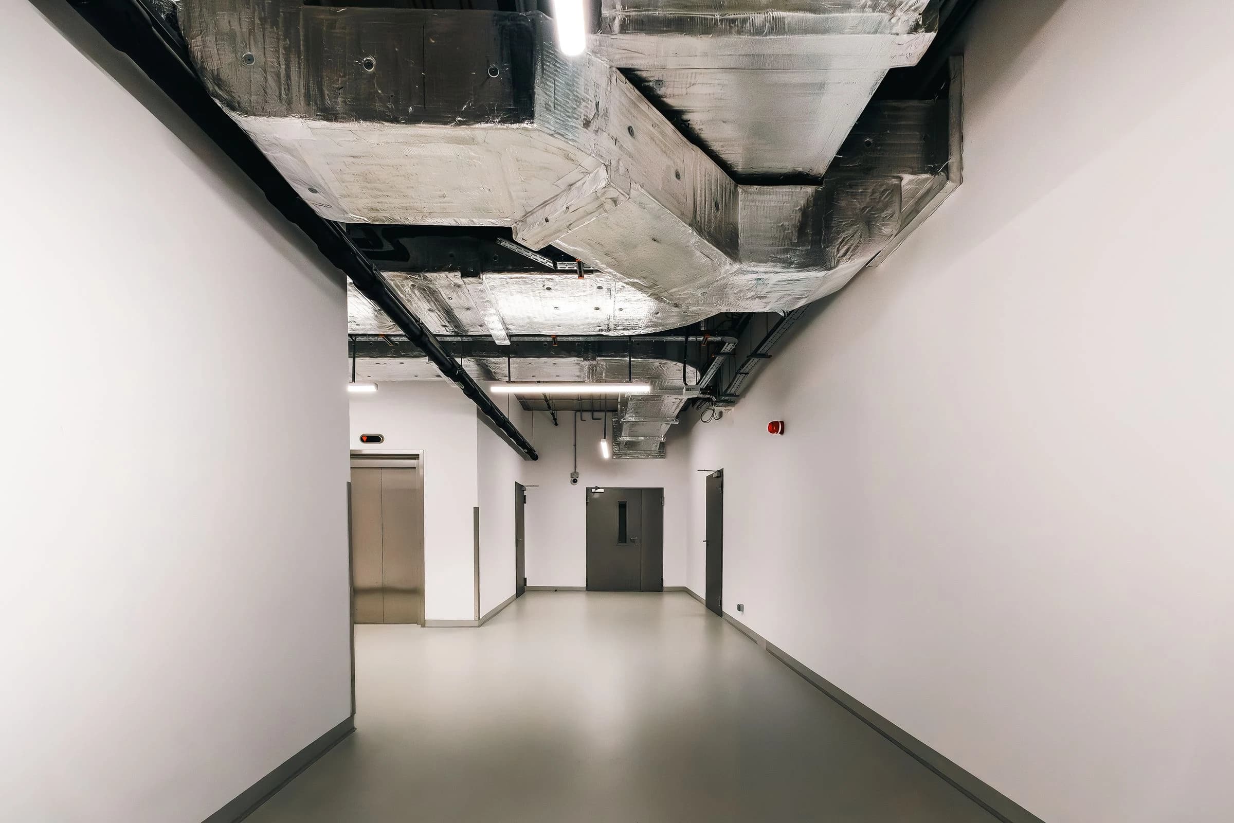 Exposed insulated HVAC ductwork coordinated with pipes and cable trays above a commercial corridor