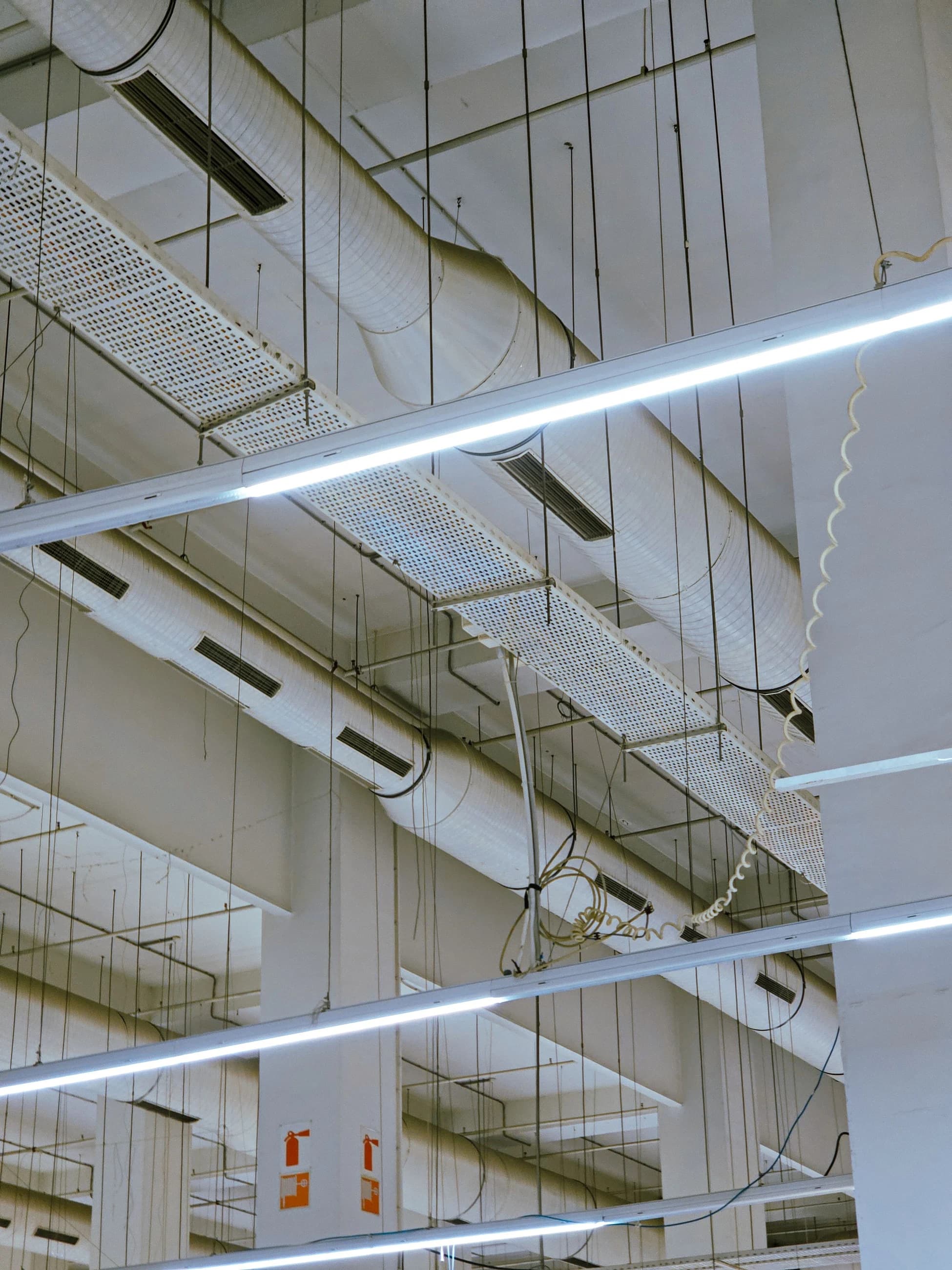 Suspended HVAC ductwork, pipes and lighting coordinated across an industrial building ceiling