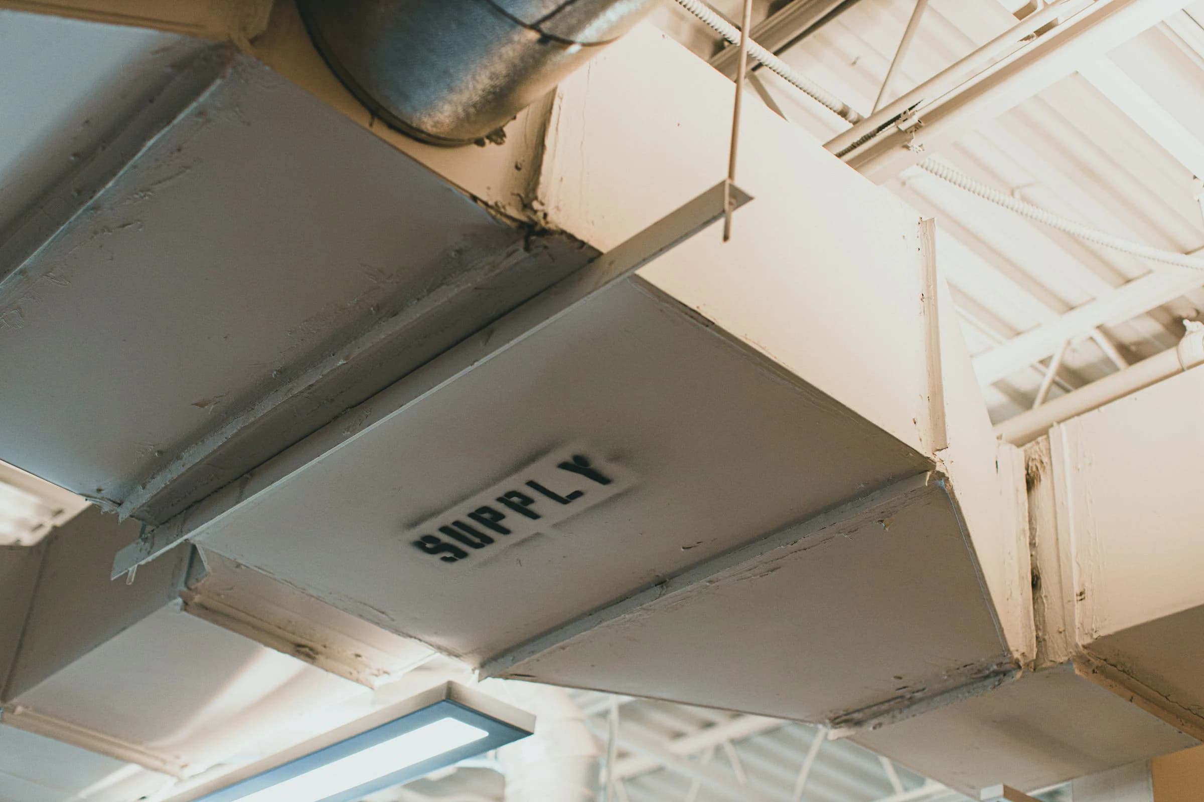 A rectangular supply-air duct and connected round duct suspended below a building ceiling