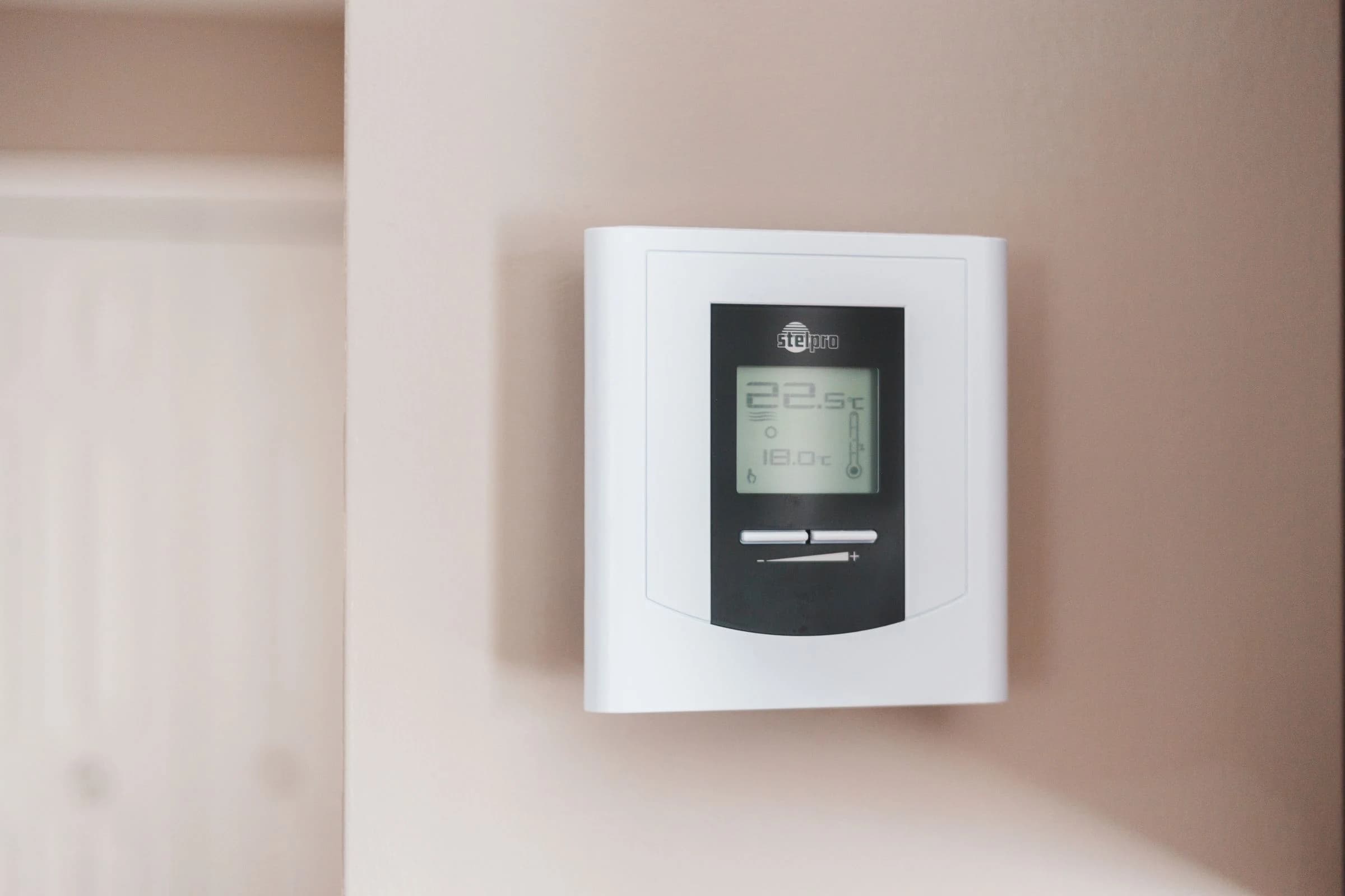 A wall-mounted digital thermostat displaying temperature settings
