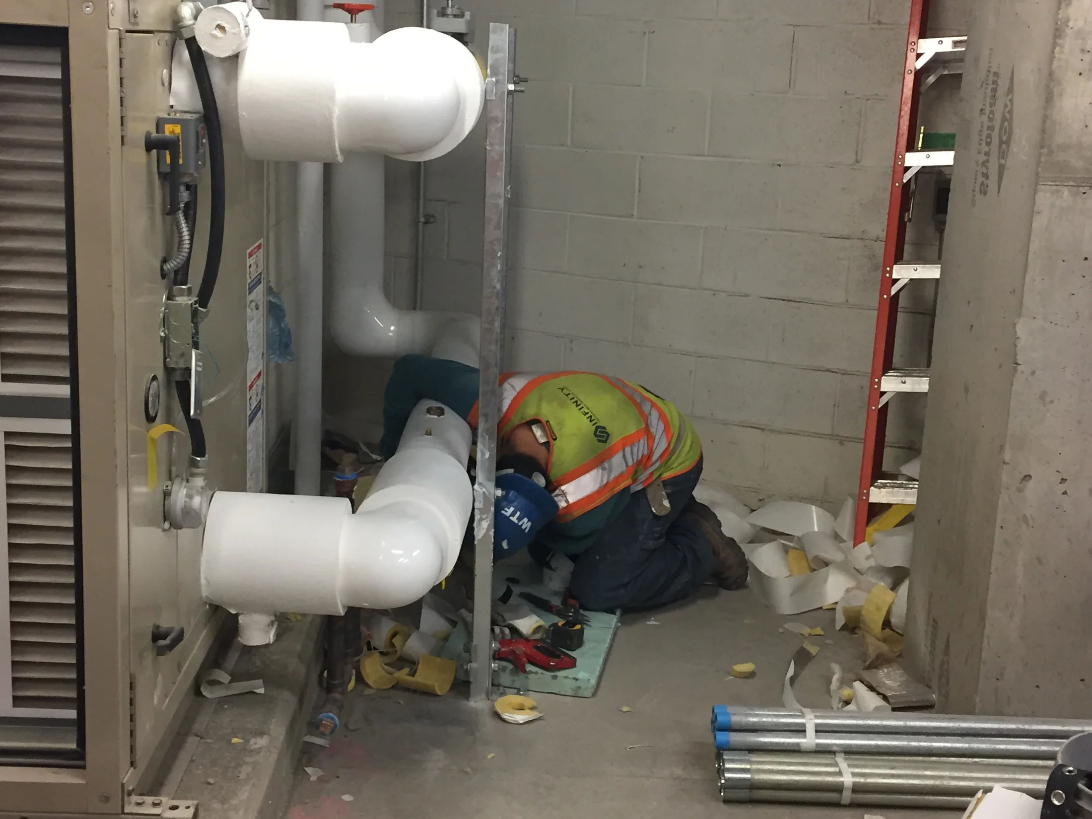 Worker installing insulation around supply and return water pipes