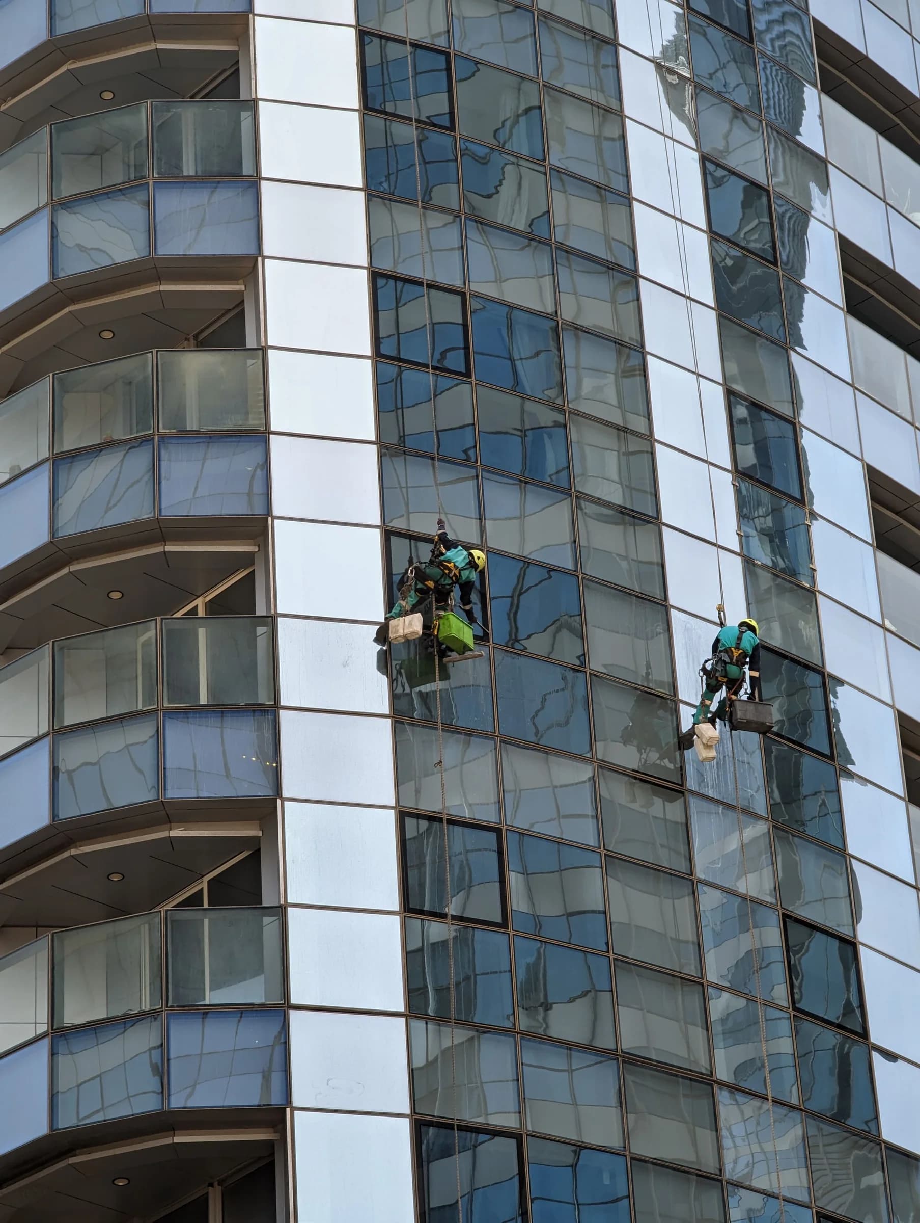Rope-access window-cleaning workers on a modern glass building in Abu Dhabi