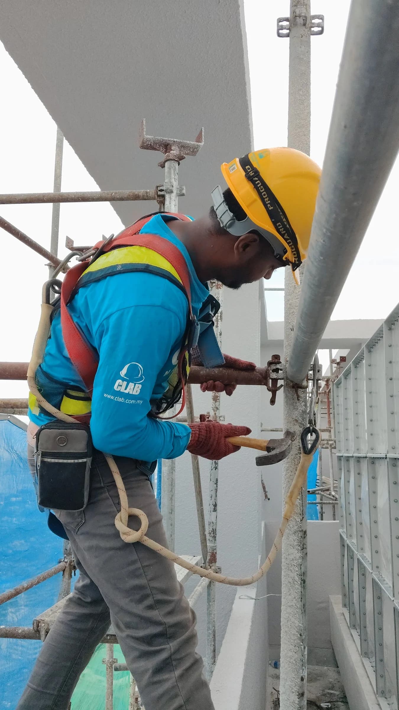 Worker wearing a hard hat and safety harness using hand tools on building scaffolding in Dubai